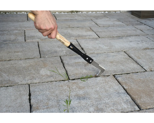 Nettoyeur de joints avec manche en bois utilisé sur des pavés.
