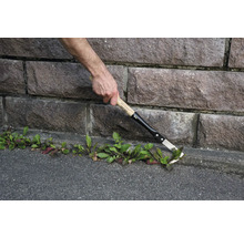 Jardinier en train d'enlever les mauvaises herbes avec un désherbeur le long d'un mur en pierre