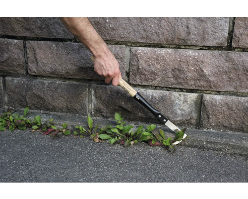 Jardinier en train d'enlever les mauvaises herbes avec un désherbeur le long d'un mur en pierre
