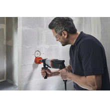 Un homme perce un trou dans un mur en béton avec une carotteuse.