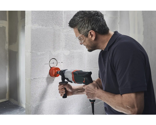 Un homme perce un trou dans un mur à l'aide d'une scie cloche.