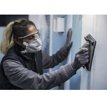 Une personne portant un équipement de protection lisse un mur avec une lisseuse.