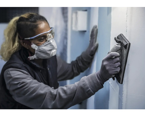 Une personne portant un équipement de protection lisse un mur avec une lisseuse.
