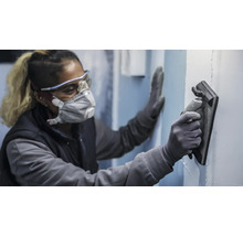 Une personne porte un équipement de protection et utilise une cale à poncer pour poncer un mur.