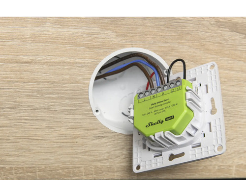 Contrôleur de gradation intelligent Shelly Dimmer Gen4 lors de l'installation dans une boîte d'encastrement avec câblage et support d'interrupteur.