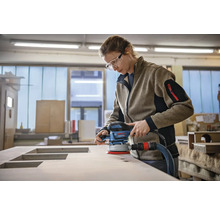 Une femme ponce une plaque de bois avec une ponceuse excentrique