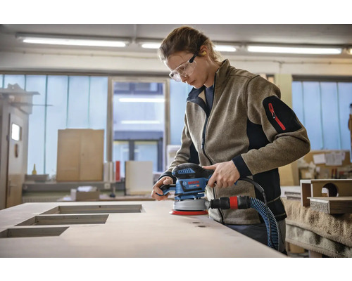 Une femme ponce une plaque de bois avec une ponceuse excentrique