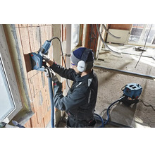 Un artisan utilise une rainureuse à murs sur un mur en briques. Un système d'aspiration de poussière est connecté.