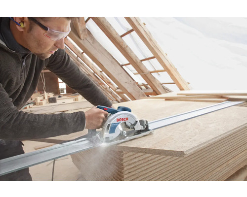 Un artisan coupe des panneaux de bois avec une scie circulaire sur un rail de guidage. Logo Bosch.