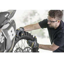 Une personne monte un pneu de moto avec des gants de travail.