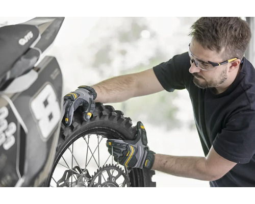 Une personne monte un pneu de moto avec des gants de travail.