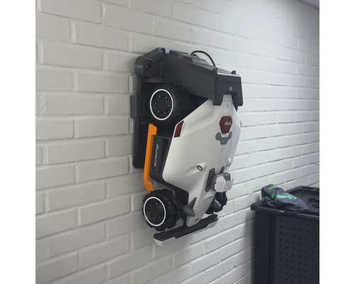 Robot tondeuse plié sur un support mural.