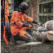 Un homme en équipement de protection scie du bois avec une tronçonneuse.