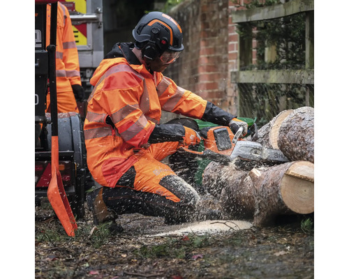Un homme en équipement de protection scie du bois avec une tronçonneuse.