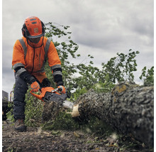 Un homme équipé de vêtements de protection et d'une tronçonneuse Husqvarna coupe un tronc d'arbre.