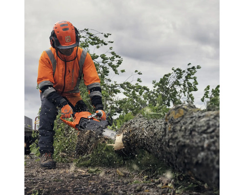 Un homme équipé de vêtements de protection et d'une tronçonneuse Husqvarna coupe un tronc d'arbre.