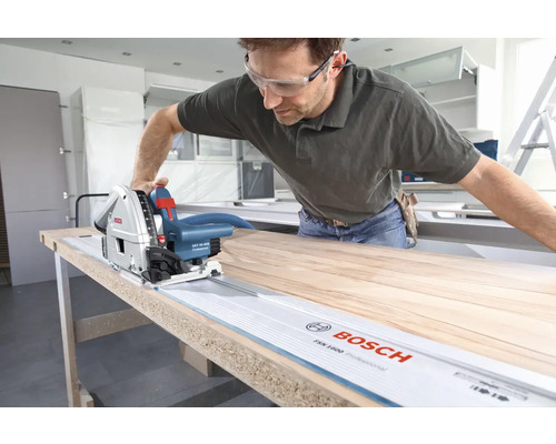 Un artisan scie une plaque de bois avec une scie plongeante Bosch et un rail de guidage.