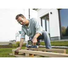 Mann mit Schutzbrille verschraubt Holzbalken mit einem Bosch Akku-Drehschlagschrauber im Garten vor einem Haus.