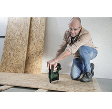 Un homme portant des lunettes de protection fixe un panneau OSB avec une agrafeuse sans fil Bosch sur une structure en bois.
