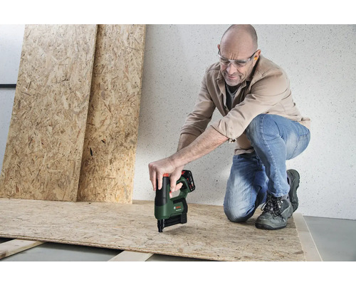 Un homme portant des lunettes de protection fixe un panneau OSB avec une agrafeuse sans fil Bosch sur une structure en bois.