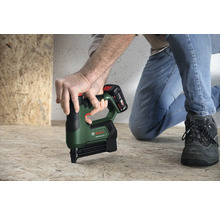 Une personne utilise une agrafeuse sans fil Bosch AdvancedTacker 18 Volt sur un panneau en bois au sol dans une pièce lumineuse.