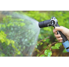 Une main tient un pulvérisateur de jardin qui arrose les plantes