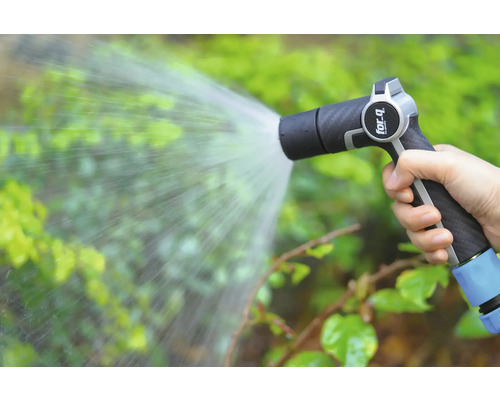 Une main tient un pulvérisateur de jardin qui arrose les plantes