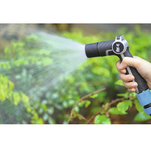 Une main tient un pistolet d'arrosage et arrose des plantes.