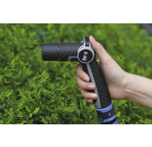 Une main tient un pistolet d'arrosage de la marque For Q devant un buisson vert