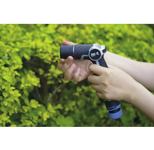 Une personne tient un pulvérisateur de jardin for_q devant un buisson vert.