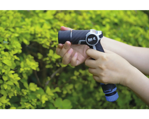 Une personne tient un pulvérisateur de jardin for_q devant un buisson vert.