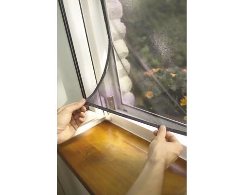 Une personne fixe une moustiquaire à une fenêtre.