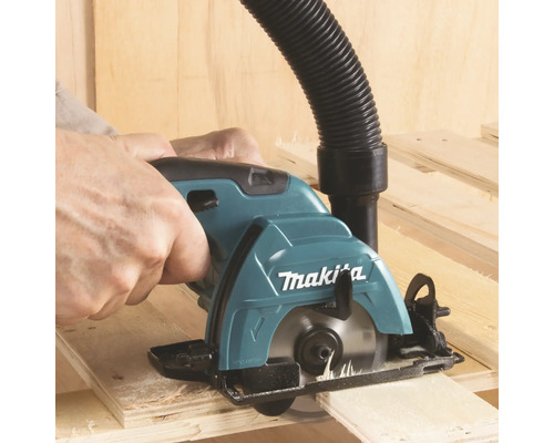 Scie circulaire portative Makita coupant du bois avec un tuyau pour aspirateur raccordé.