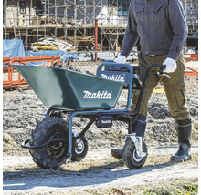Une personne pousse une brouette à batterie Makita remplie de terre sur un chantier. Appareil bleu à trois roues et Makita Logo.