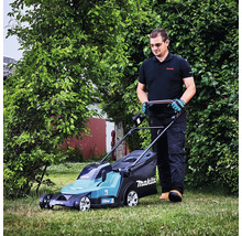 Un homme tond la pelouse dans un jardin avec une tondeuse à gazon sans fil Makita.