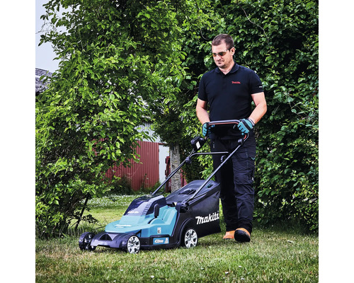 Un homme tond la pelouse dans un jardin avec une tondeuse à gazon sans fil Makita.