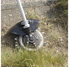 Rotations-Unkrautbürste mit Metallklingen im Einsatz auf einer Rasenfläche mit trockenem Gras.