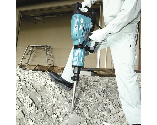 Makita Abbruchhammer wird von einer Person in Arbeitskleidung auf einem Haufen aus Betonschutt verwendet.