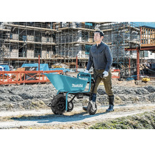 Ouvrier poussant une brouette à batterie Makita sur un chantier de construction avec des échafaudages.