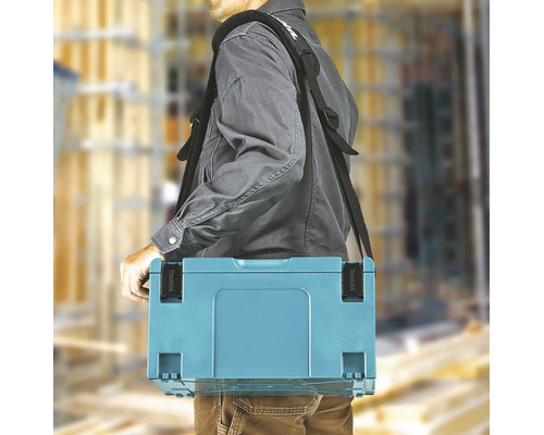 Une personne porte un coffret à outils Makita avec une bandoulière rembourrée sur un chantier lumineux. Makita Logo.