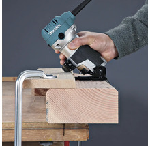 Une personne utilise une affleureuse Makita pour travailler le bord d'une planche en bois fixée sur un établi.