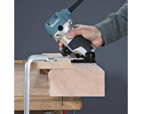 Une personne utilise une affleureuse Makita pour travailler le bord d'une planche en bois fixée sur un établi.