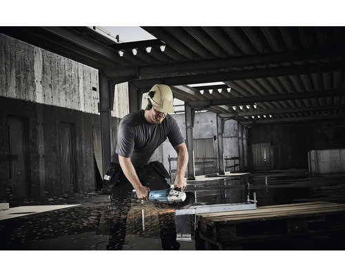 Bauarbeiter mit Helm und Gehörschutz schneidet mit einem Makita Winkelschleifer Metall auf einer Baustelle, Funkenflug.