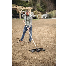 Mann ebnet Boden mit einer Einebnungsharke.