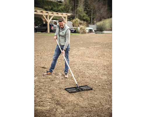 Mann ebnet Boden mit einer Einebnungsharke.