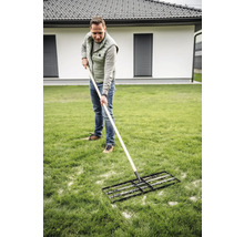 Ein Mann verwendet eine Rasenwalze zur Rasenpflege im Garten.