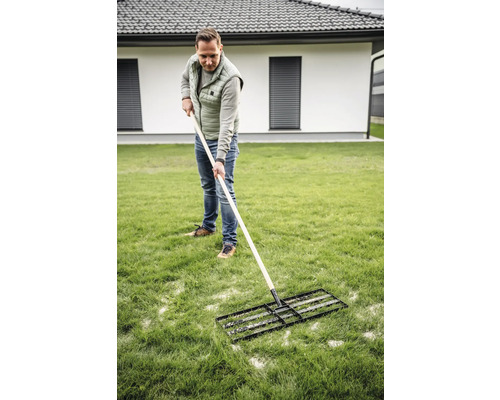 Ein Mann verwendet eine Rasenwalze zur Rasenpflege im Garten.