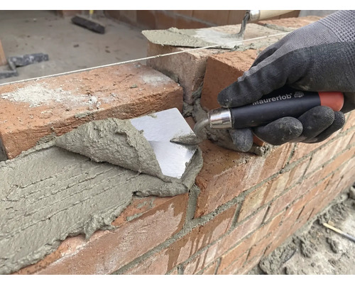 Maçon pose une brique avec une truelle sur un chantier