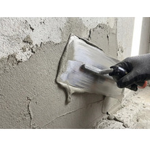 Eine Person glättet Putz mit einer Glättkelle an einer Wand.