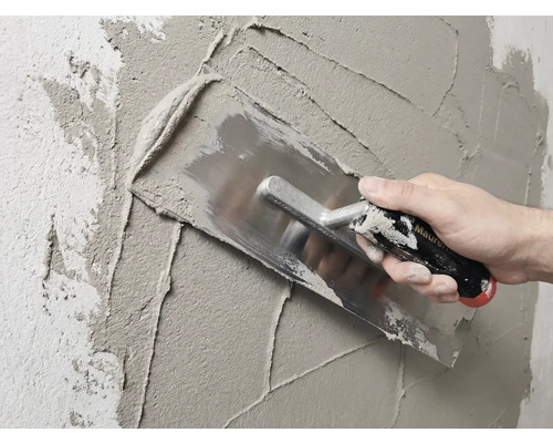 Maçon enduisant un mur avec une taloche